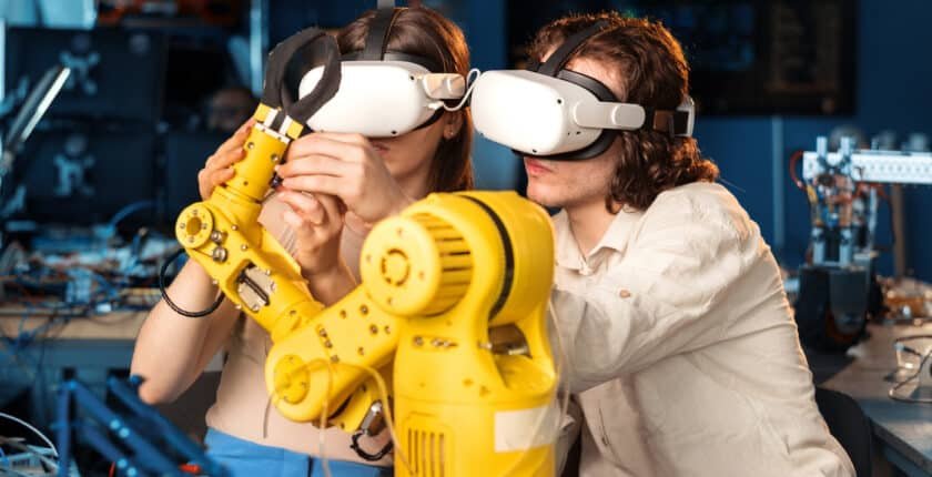 Hombre y mujer jóvenes con gafas VR haciendo experimentos en robótica en un laboratorio. Robot y herramientas sobre la mesa.